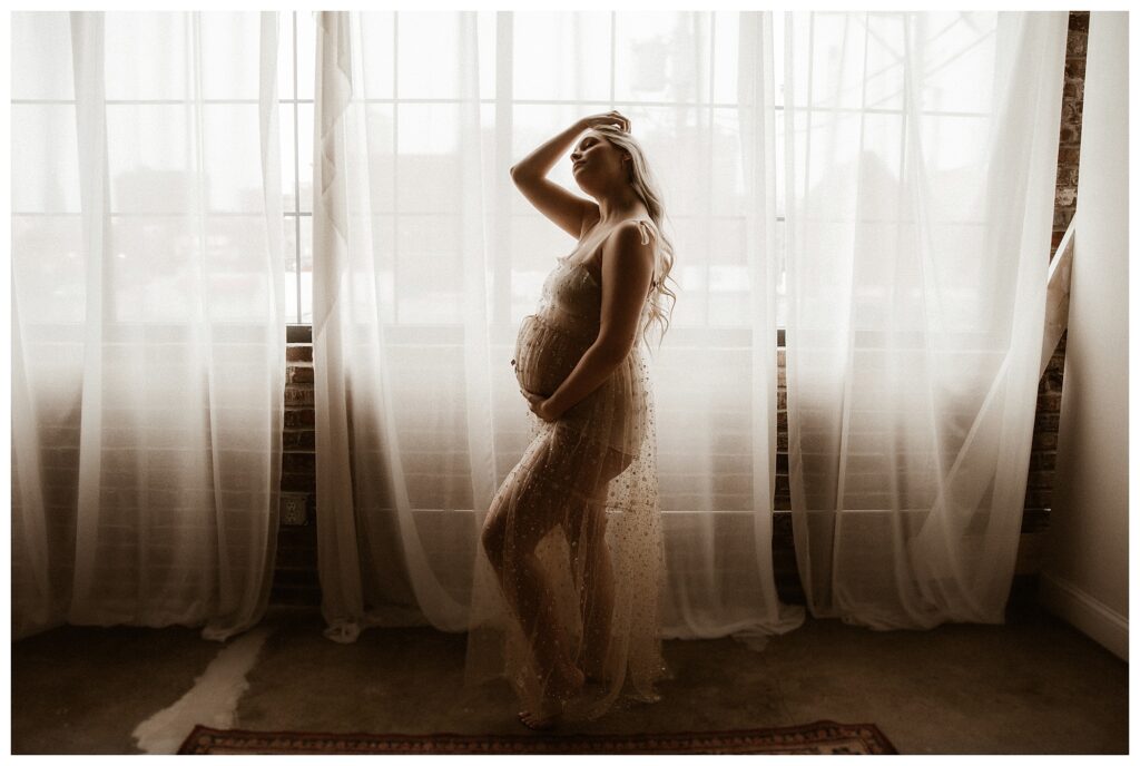 Studio Maternity session mom moving her hair in front of sheer curtain wall brick studio rustic fine art photography Saint Louis Missouri