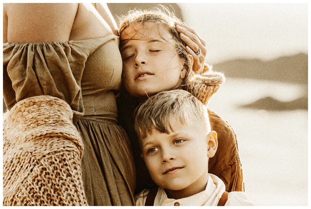 Close up of mother snuggling with her daughter and son in windy beach session at Oregon workshop with at Stormy Solis Rebecca Stephenson fine art family photographer St Louis Missouri