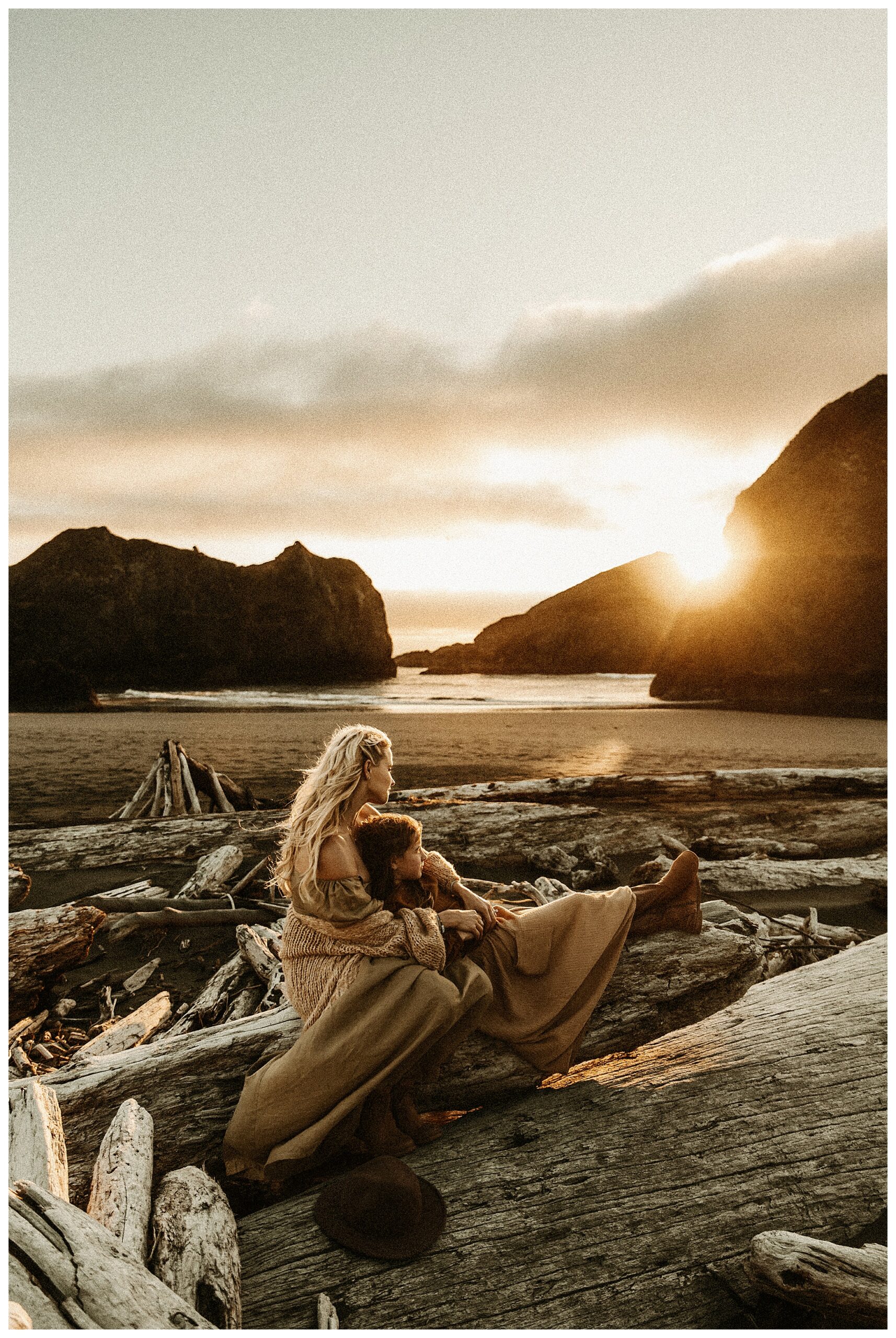 mother and daughter sitting on driftwood log at Oregon Coast with sun setting behind them at Stormy Solis workshop Rebecca Stephenson fine art family photographer St Louis Missouri