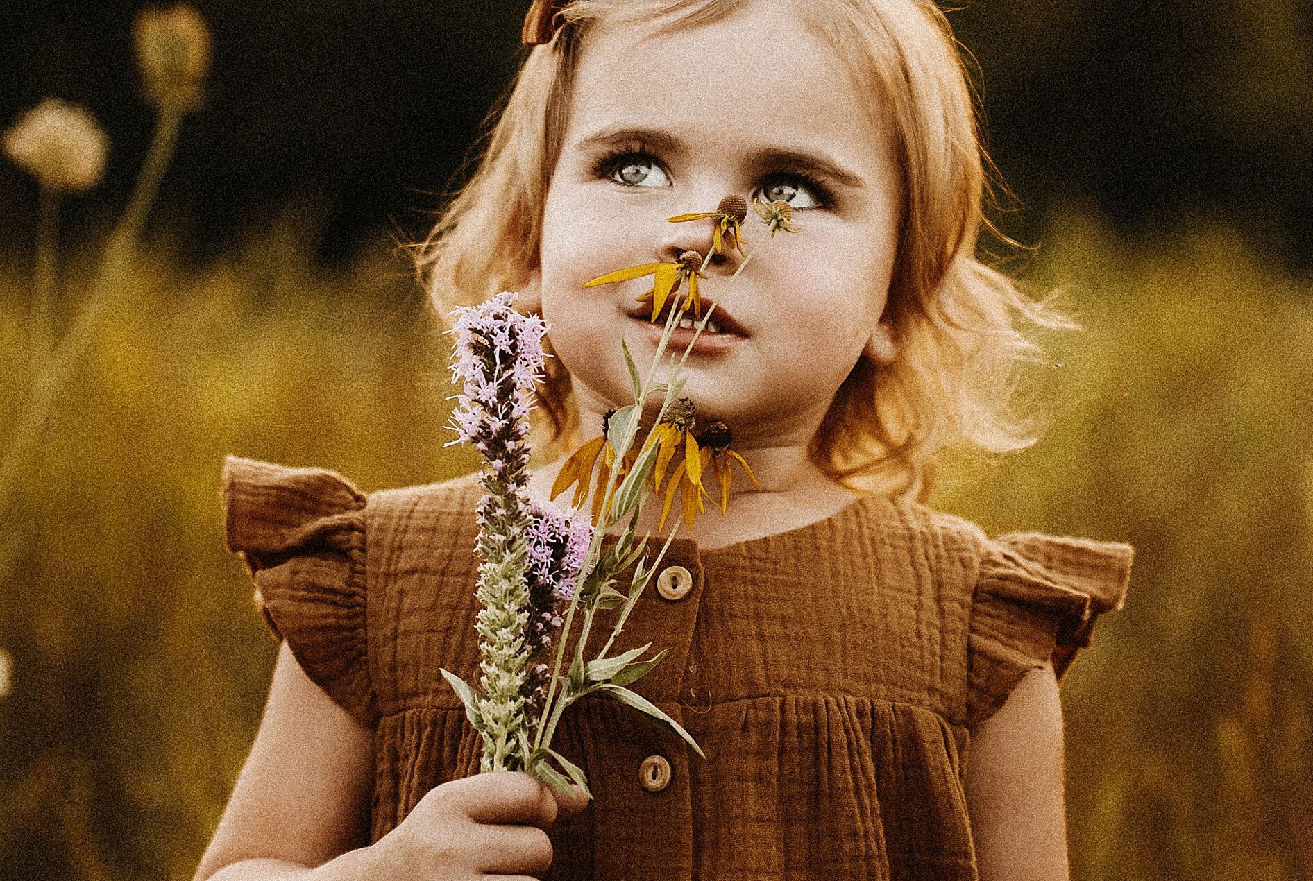 Girl smelling wildflowers during outdoor fun family session fine art childrens portraits Missouri