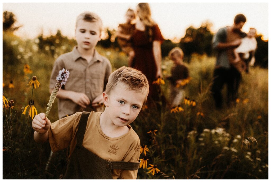 Family of seven walking through wildflower field during outdoor family session in Missouri sunset
