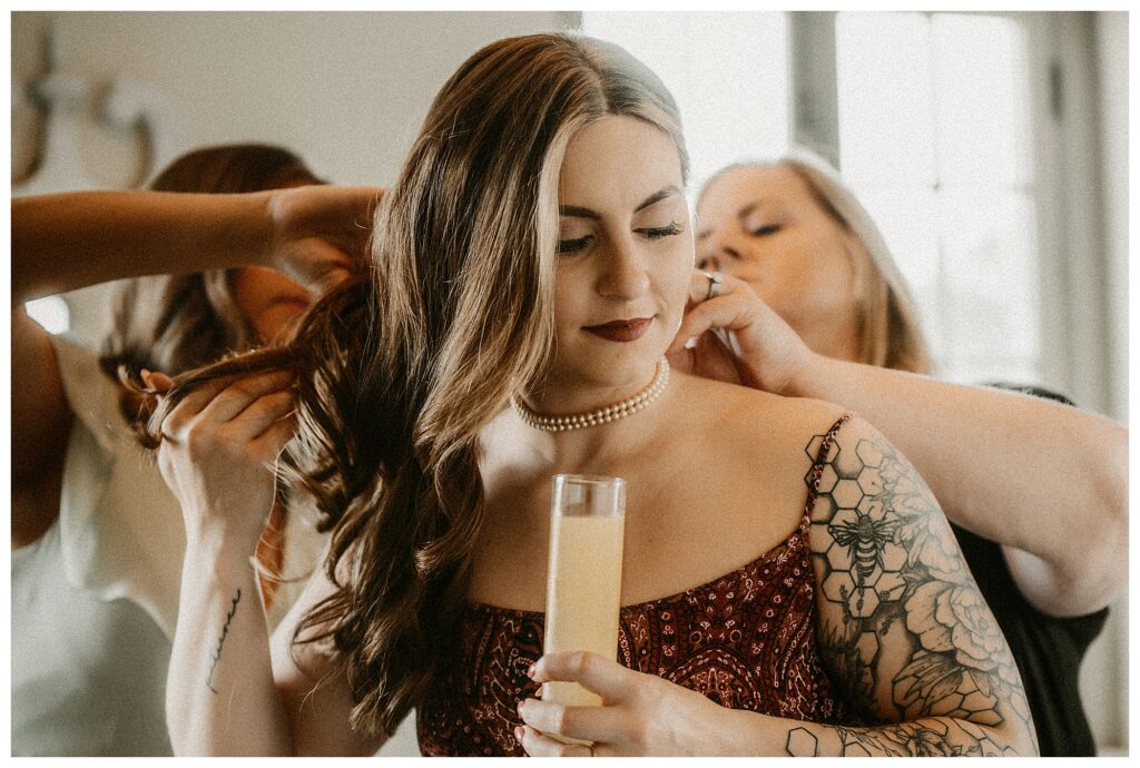 Bride putting on pearl necklace and holding Mimosa at St Louis das Bevo wedding venue