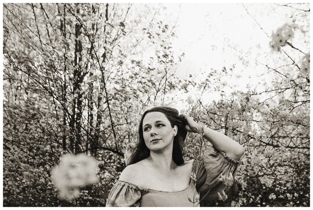 black and white photo of pregnant woman between blooming trees at outdoor session in St Charles Missouri