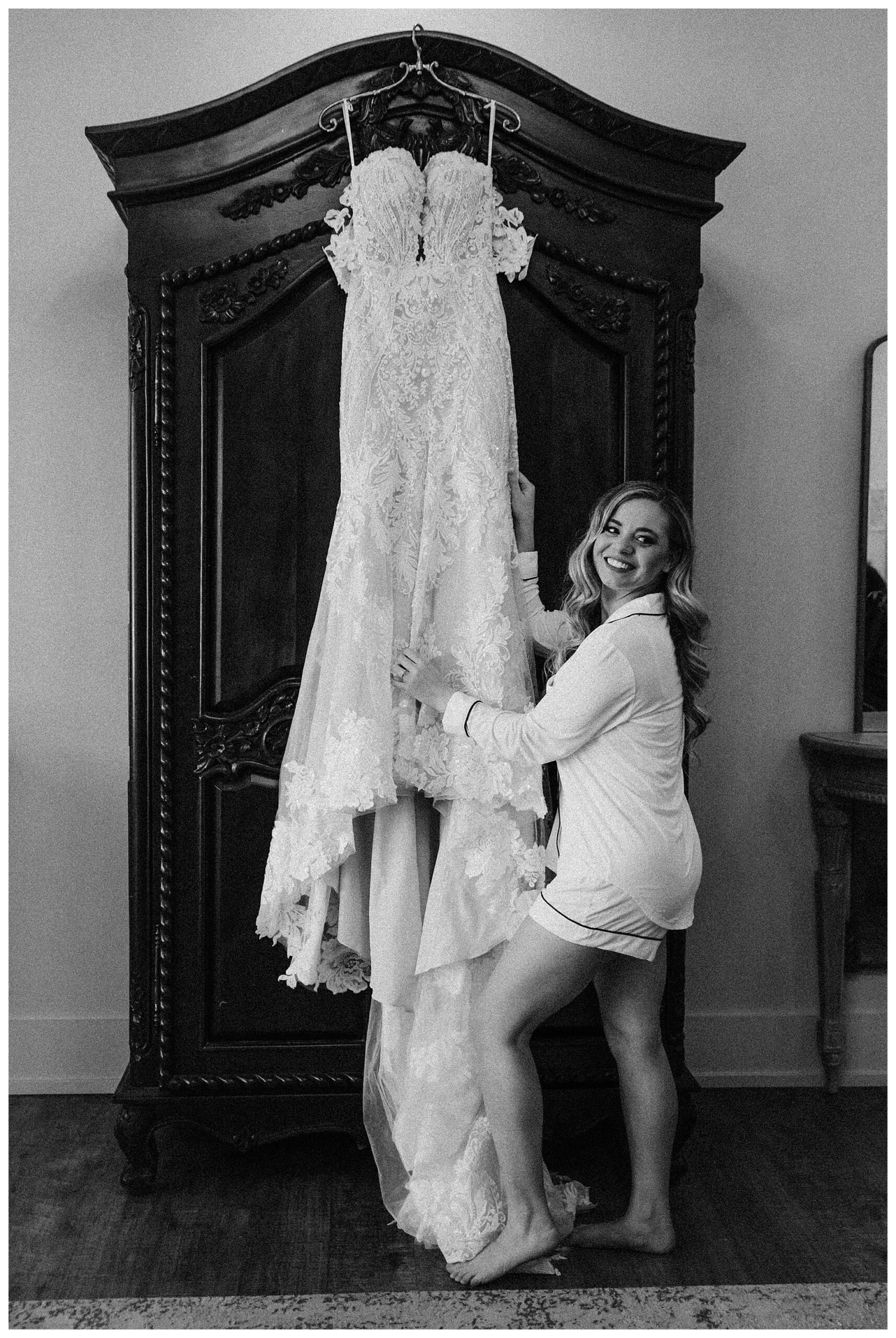 bride in front of wedding gown hanging up in bridal suite