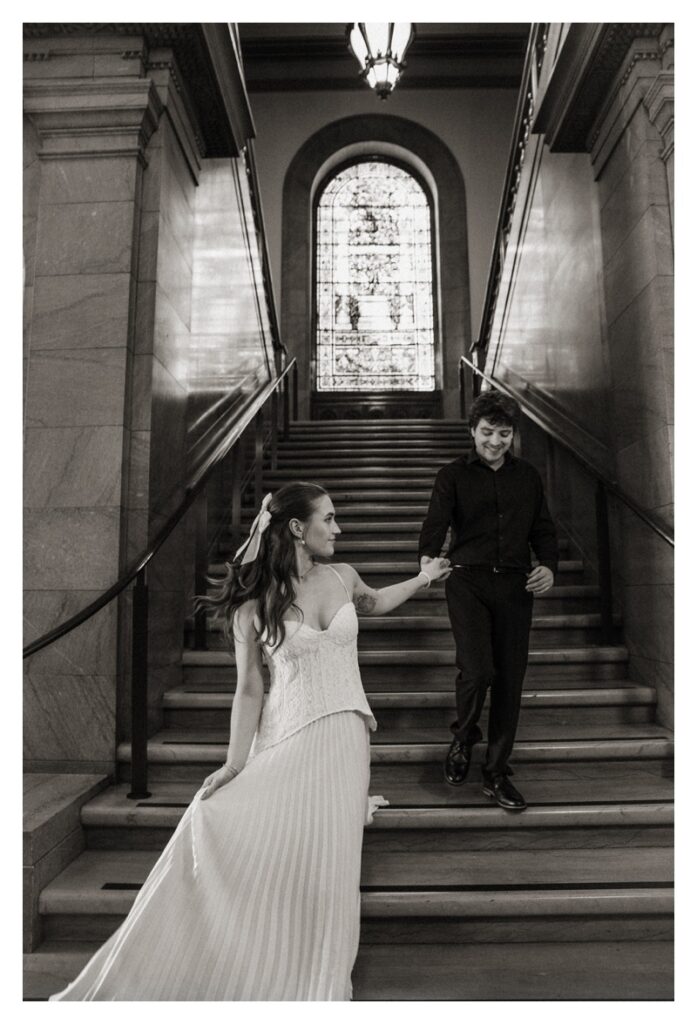 black and white engagement photo of couple walking down staircase of vintage library St. Louis Missouri